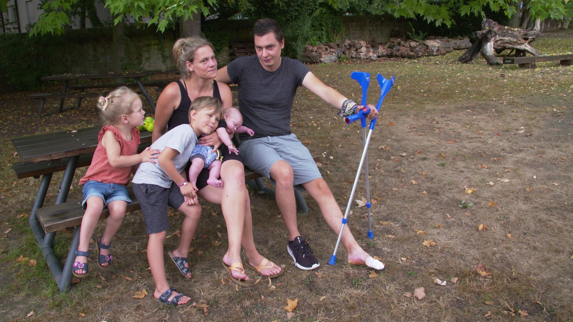 "37°: Zuhause gesucht - Wohnungslose Familien in Deutschland": Ein dreijähriges Mädchen, ein sechsjähriger Junge lachen, sie kuscheln sich auf einer Bank aneinander, der kleine Junge lehnt sich an ein schlafendes Baby, das auf dem Schoß seiner Mutter sitzt. Die Mutter freut sich über die Kinder und lehnt neben ihrem Mann. Der Mann schaut ernst.