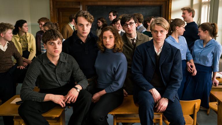 "Das schweigende Klassenzimmer": Erik Babinsky (Jonas Dassler), Theo Lemke (Leonard Scheicher), Lena (Lena Klenke), Paul (Isaiah Michalski) und Kurt Wächter (Tom Gramenz) sitzen zusammen auf den Tischen in ihrem Klassenzimmer und schauen nach vorne.