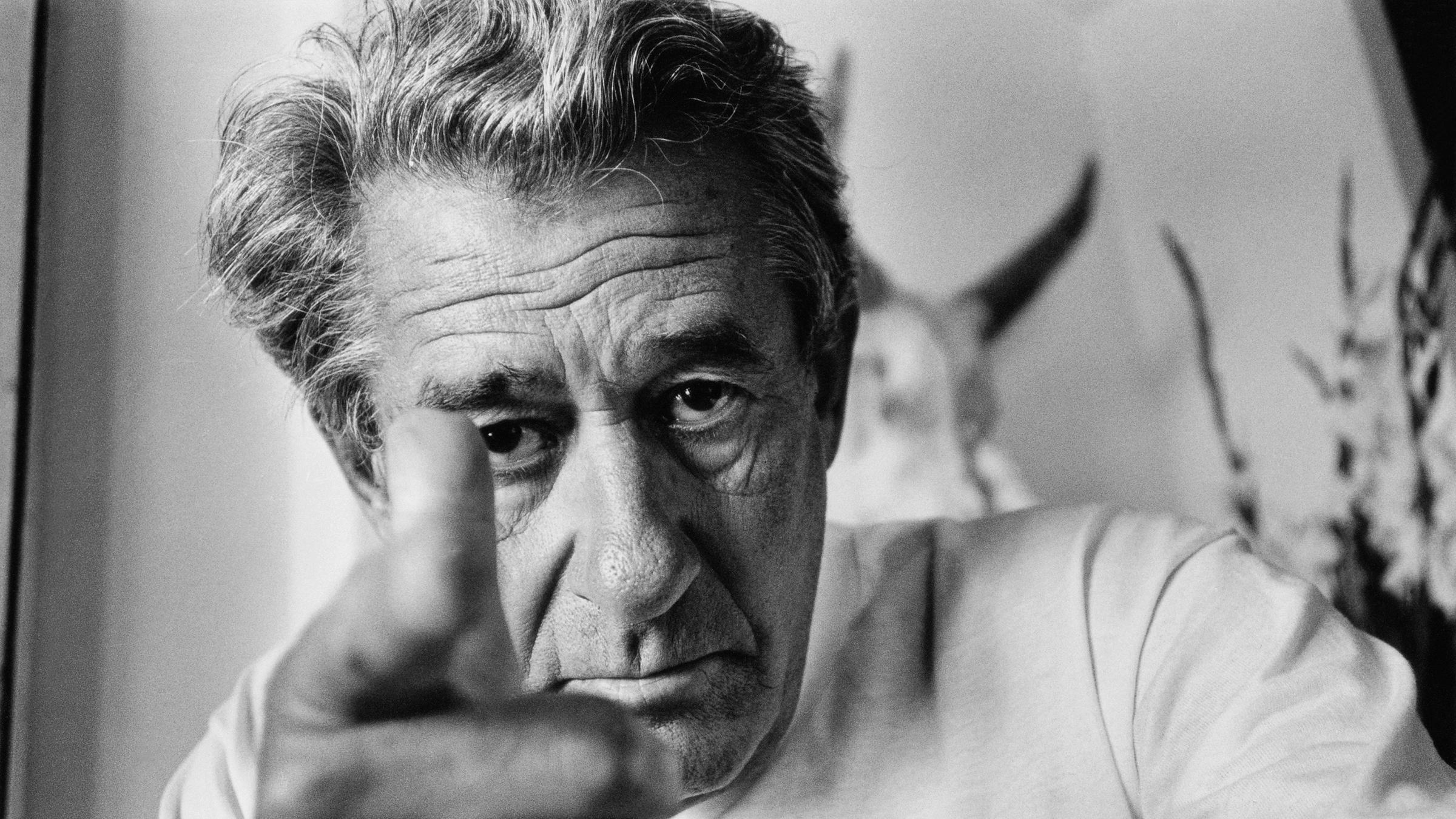 "Helmut Newton - The Bad and the Beautiful": Auf dem schwarz-weiß Bild sieht man den Fotografen Helmut Newton,  er schaut direkt in die Kamera und zeigt mit seinem rechten Zeigefinger direkt auf den Betrachter