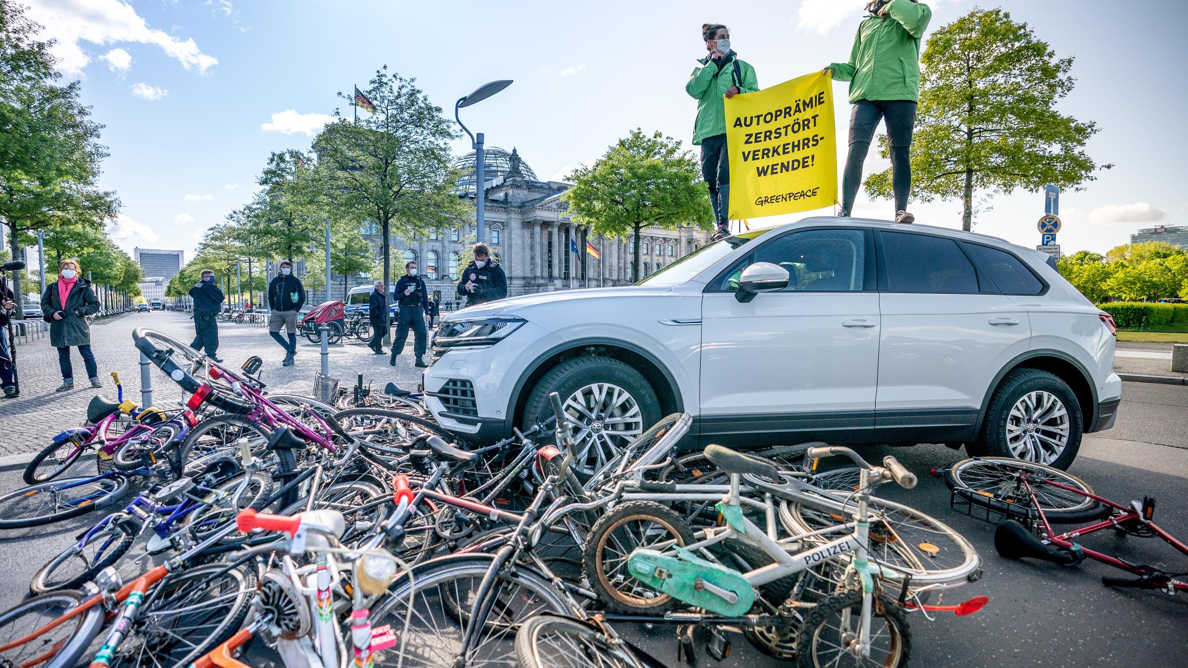 "Auto Macht Deutschland - Die Autoindustrie und ihre Politik": Zwei Demonstranten auf einem SUV, unter dem viele Fahrräder liegen.