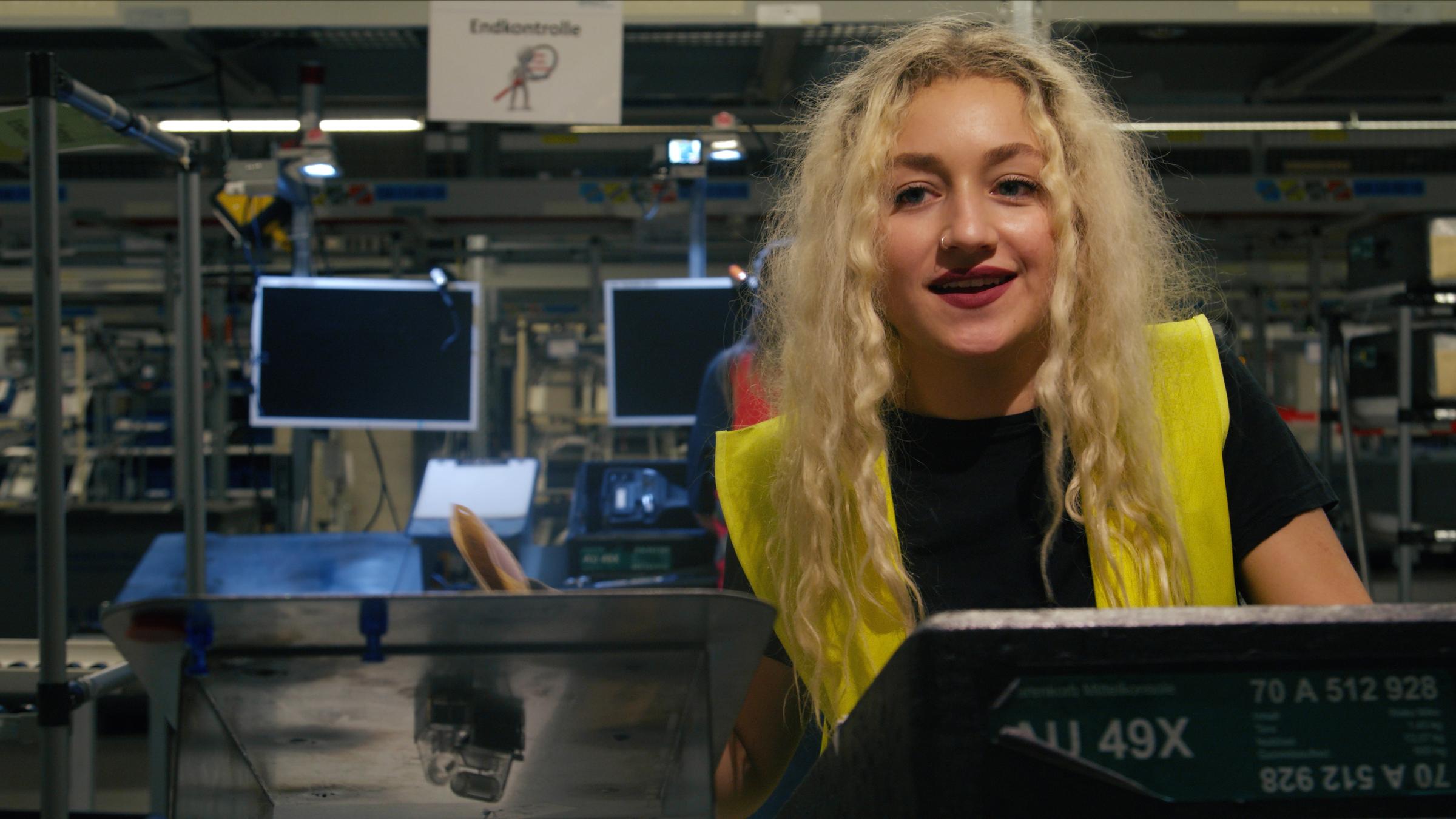 "Ab 18! - Seda baut Autos": Nahaufnahme von blondem Mädchen, das an einem Schalter steht und lacht.