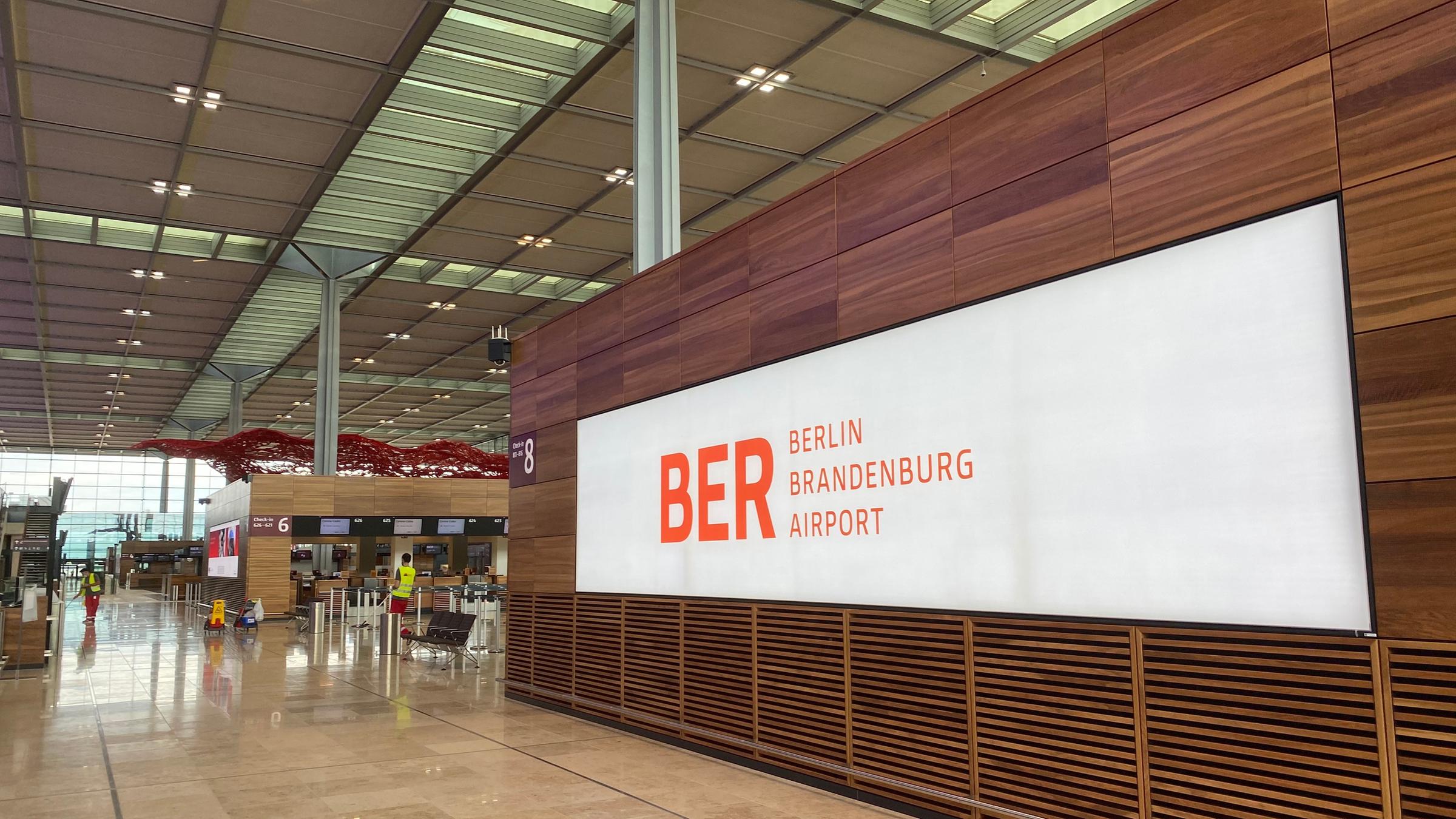 "ZDF.reportage: Flughafen Berlin - Der Pannen-Airport BER geht an den Start": Innenansicht Terminal mit Schriftzug BER Berlin Brandenburg Airport. Im Hintergrund Arbeiter mit gelben Westen.