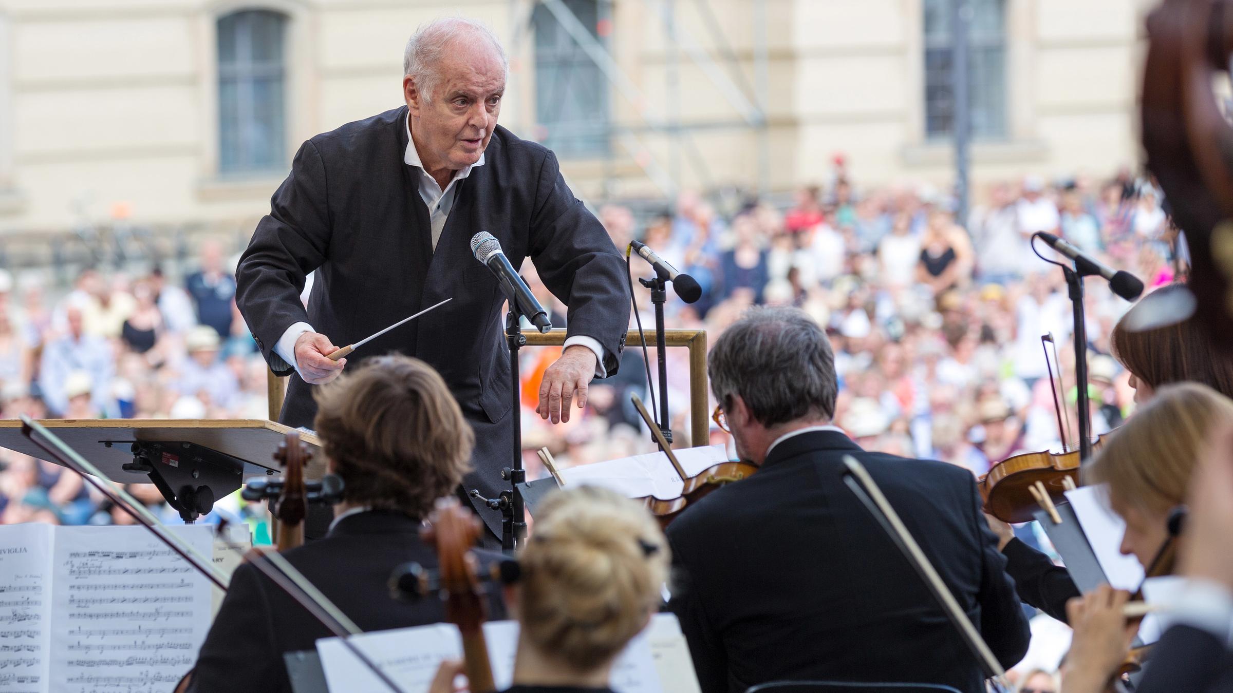 "Berlin feiert Beethoven":  Daniel Barenboim steht leicht gebeugt vor dem Orchester und dirigiert ein Open-Air Konzert. Im Hintergrund ist verschwommen Publikum zu erkennen.