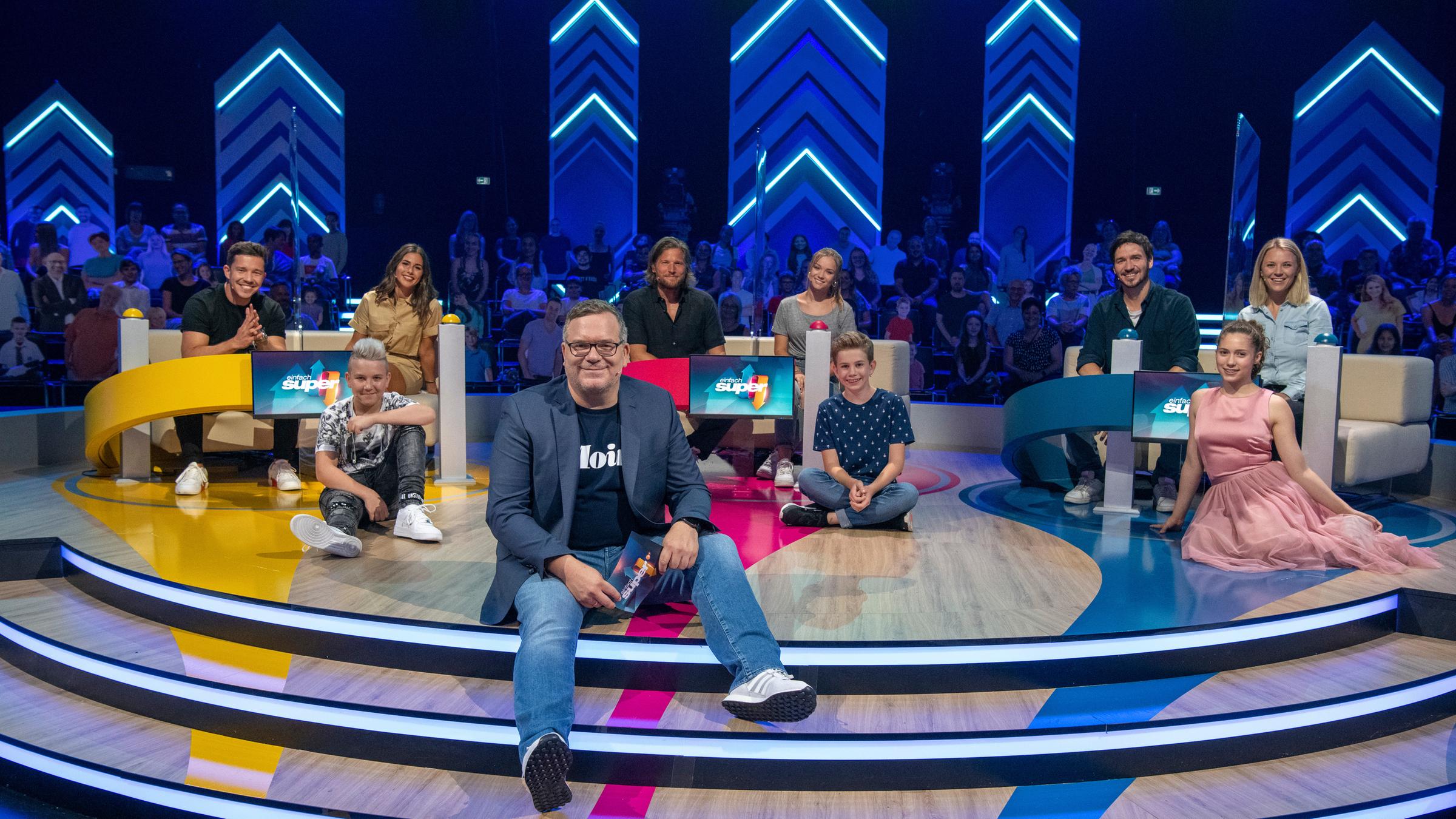 "Einfach super!": Die drei Teams von "Einfach super!": Nico Santos, Sarah Lombardi und Lukas, Sebastian Ströbel, Julia Beautx und Maxl  und Felix Neureuther, Miriam Neureuther und Feena. Die Promis sitzen hinter ihren Pulten. Die  Kinder sitzen vor ihrem jeweiligen Promi-Team. Ganz vorne sitzt Elton