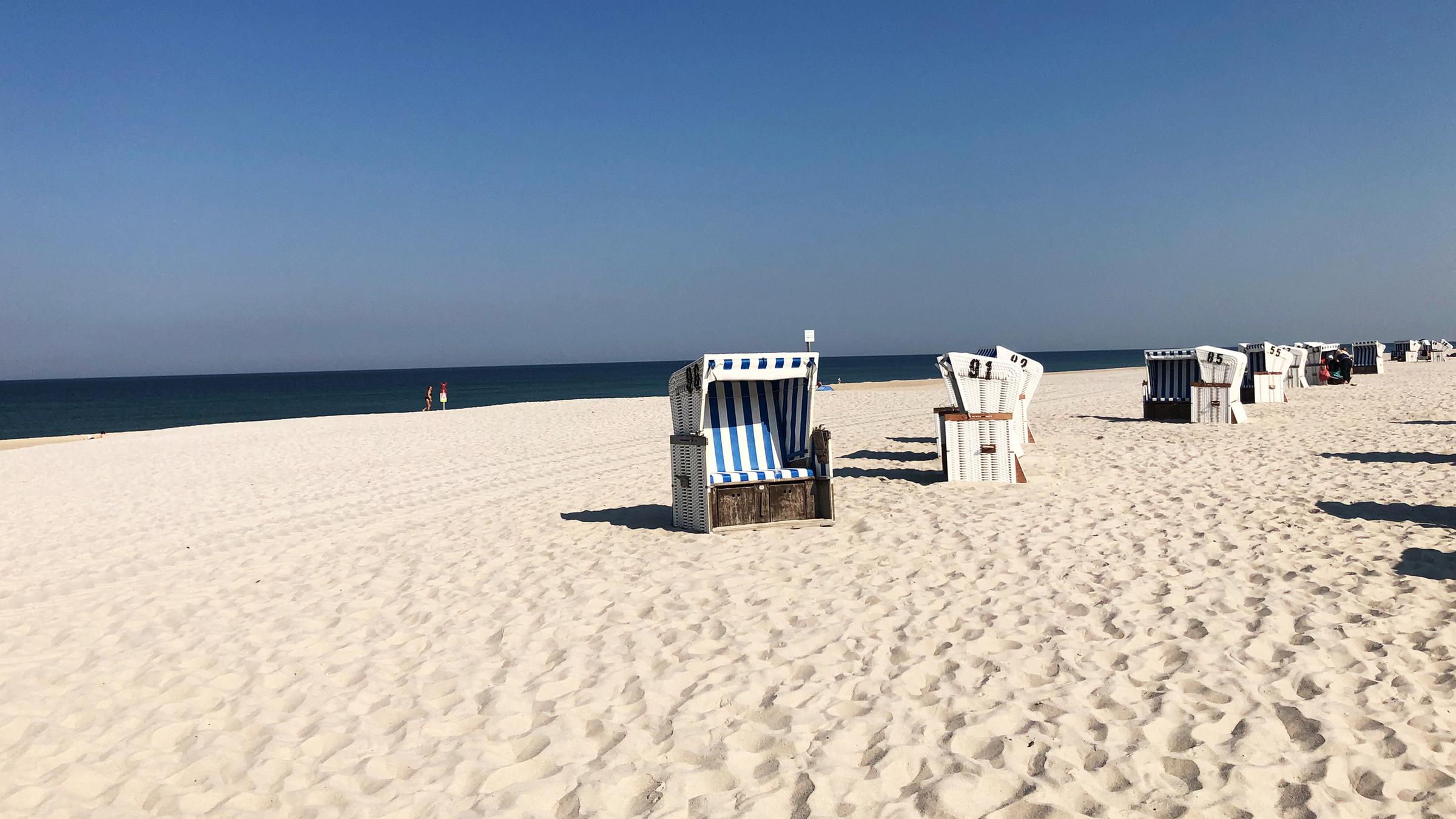 "Sylt - Deutschlands edles Nordlicht": Ein weißer, weiter Strand mit Strandkörben darauf. Im Hintergrund das Meer und blauer Himmel.