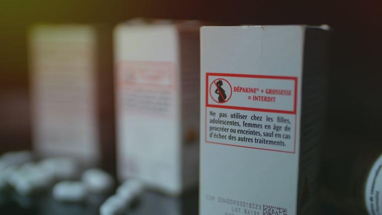 "Big Pharma - Die Macht der Konzerne": Drei Schachteln des Medikaments Dépakine, versehen mit einem rot-schwarzen Icon, das eine durchgestrichene Schwangere zeigt. Daneben liegen einige lose Tabletten.