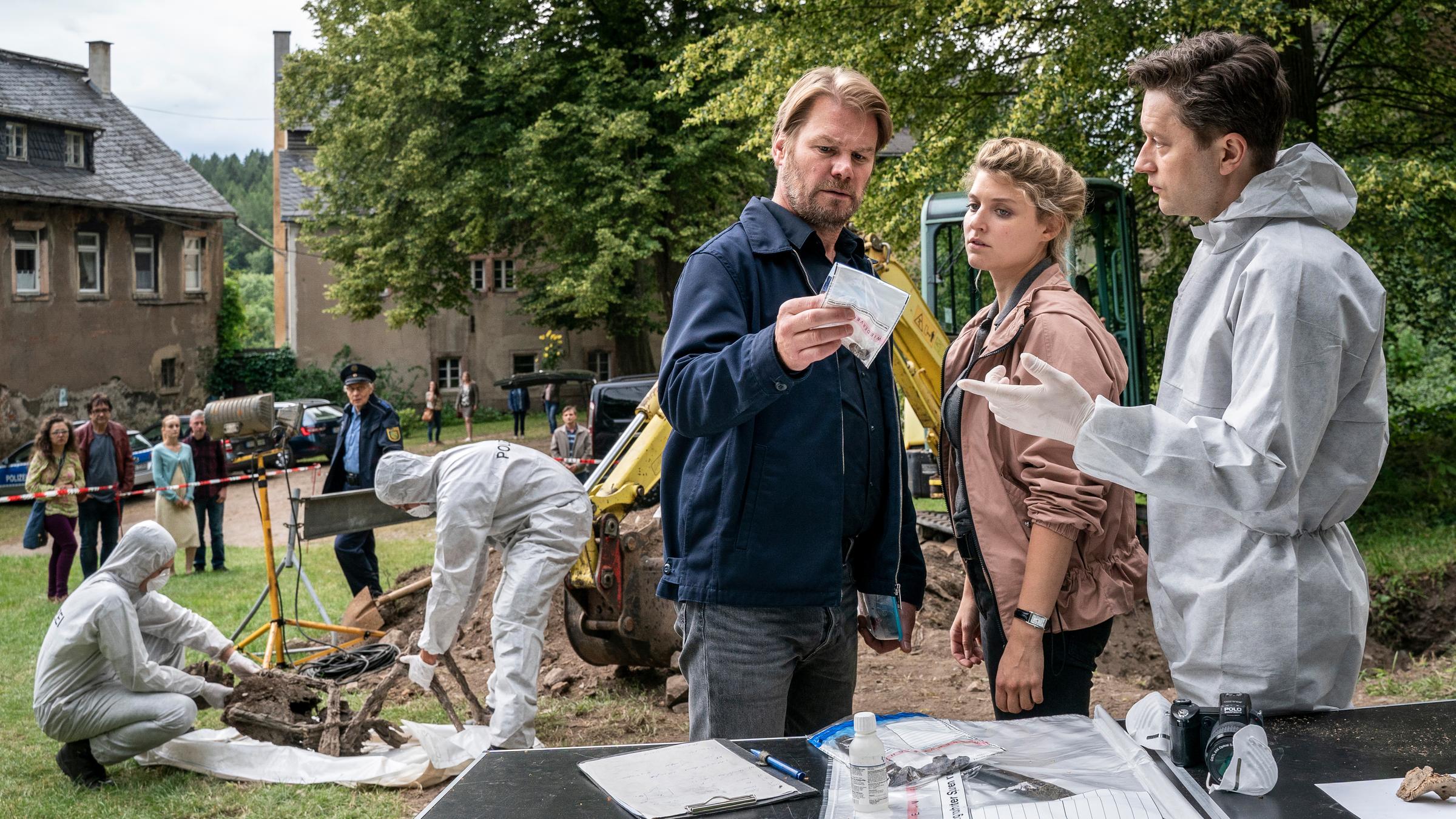 "Erzgebirgskrimi - Der Tote im Burggraben": Während zwei KTU-Beamten (Komparsen) die verwitterte Leiche bergen,  unterrichtet Maik (Adrian Topol, r.) die Kommissare Robert Winkler (Kai Scheve,l.) und Karina Szabo (Lara Mandoki, M.) im Vordergrund über den Fund.