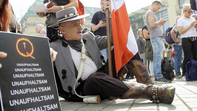 "ZDFzoom: Angriff von rechts": Ein Demonstrant sitzt auf einer Querdenken-Kundgebung neben einem Plakat, auf dem in immer größer werdender Schrift steht: "UNAUFHALTSAM". Weitere Demonstranten stehen um ihn herum.