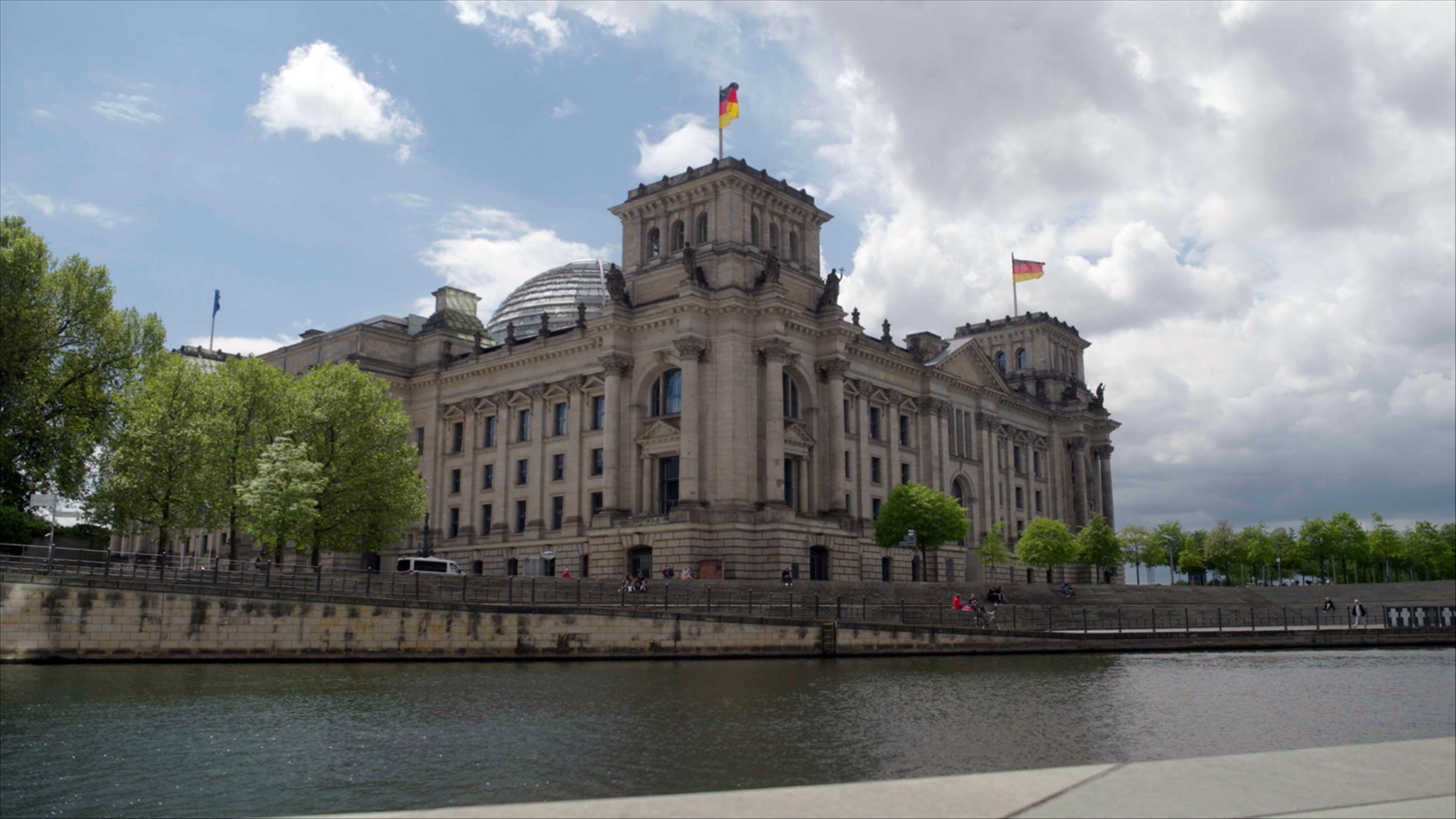 "ZDFzeit: Volksparteien ohne Volk? Die rätselhaften Wechselwähler": Blick auf das Reichstagsgebäude vor wolkigem Himmel im Sommer vom gegenüberliegenden Spreeufer.
