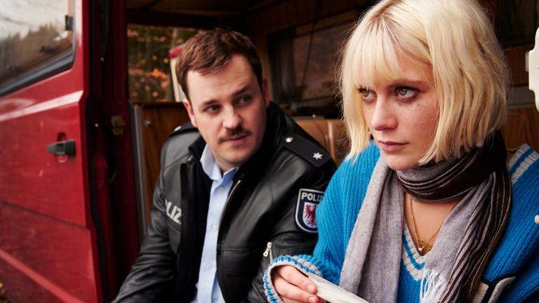 "Wir können nicht anders": Frank (Frederic Linkemann) und Edda (Alli Neumann), die eine Zigarette dreht, sitzen an Seitentür von Wohnmobil.