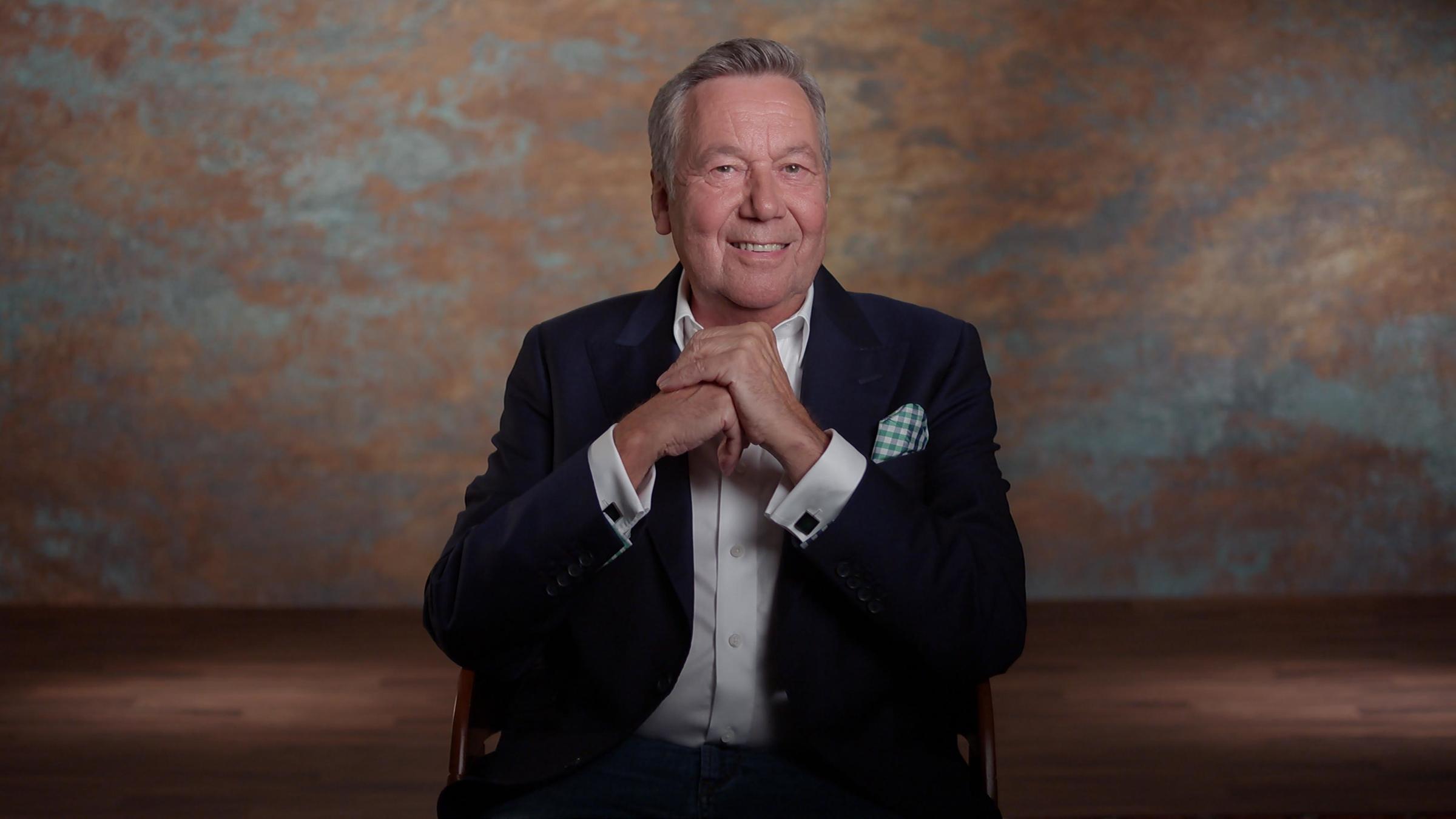 "ZDFzeit: Mensch! Roland Kaiser - Vom Findelkind zur Kultfigur": Roland Kaiser sitzt auf einem Stuhl und lacht in die Kamera.