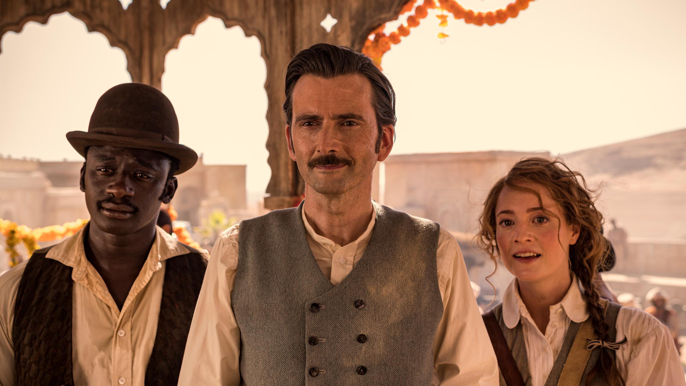 "In 80 Tagen um die Welt (4)": Phileas Fogg (David Tennant), Abigail Fix (Leonie Benesch) und Passepartout (Ibrahim Koma) stehen nebeneinander unter dem Dach eines indischen Pavillons.