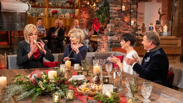 "Heiligabend mit Carmen Nebel": Der als "Karen Nebel" verkleidete Matze Knop, Carmen Nebel, Francine Jordi und Patrick Lindner sitzen in weihnachtlicher Kulisse an einem Tisch. Matze Knop spielt auf einer Flöte, Carmen Nebel auf einer Triangel und Francine Jordi sowie Patrick Lindner klatschen dazu.