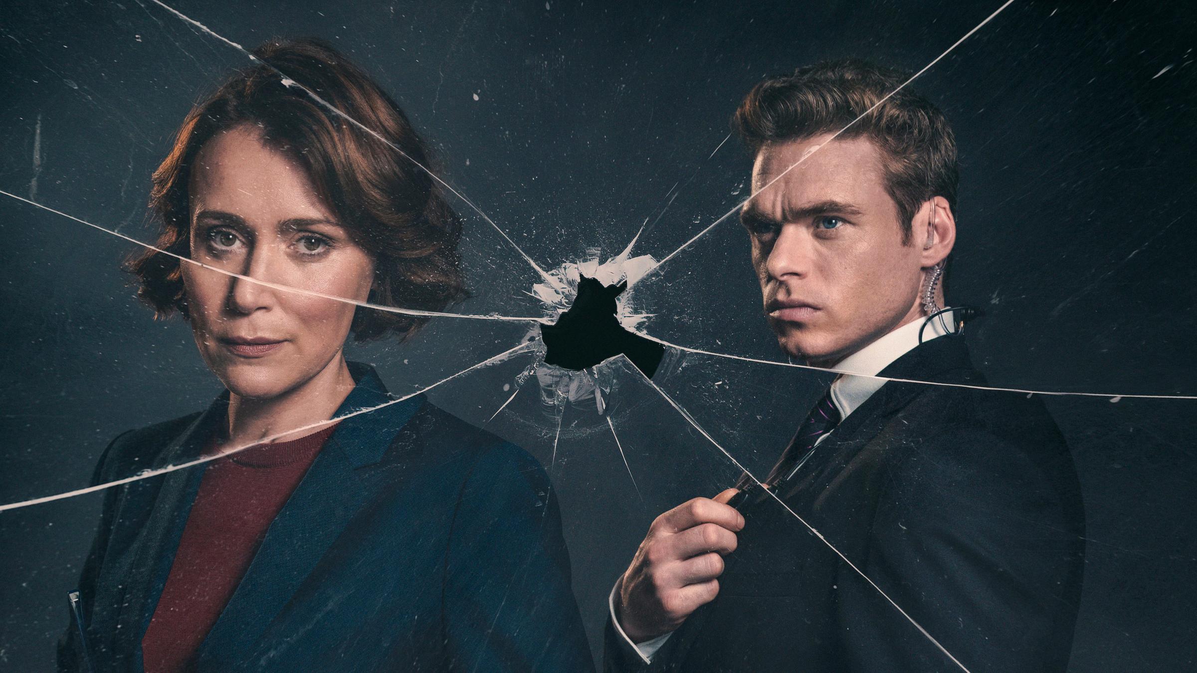 "Bodyguard (1)": "Bodyguard": Julia (Keeley Hawes) und David (Richard Madden) stehen hinter einer gesprungenen Glasscheibe, die ein Einschussloch in der Mitte hat. David hat sein Funkgerät in der Hand.