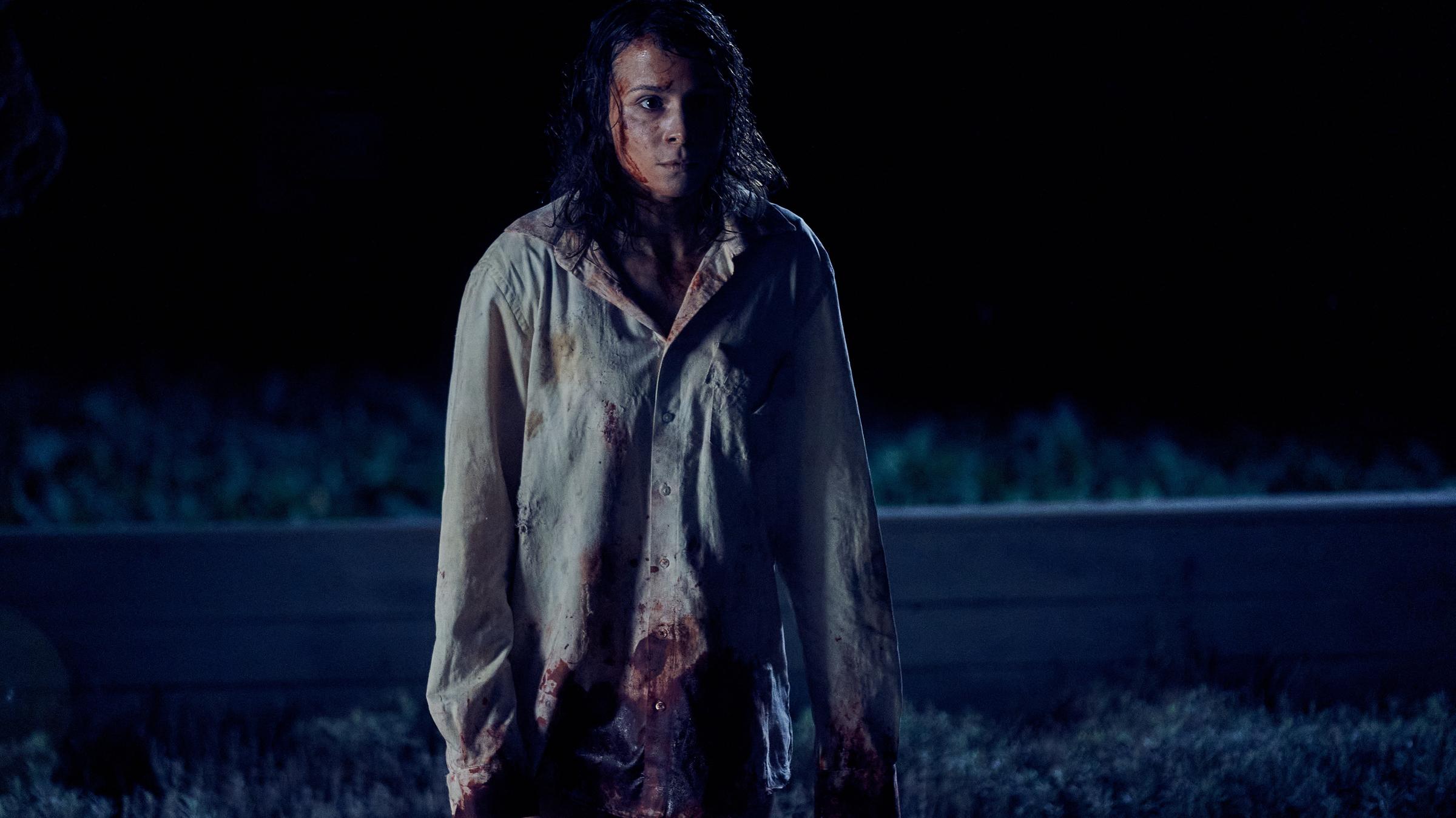 "Unbroken - Kapitel 1": Alex (Aylin Tezel) steht im Dunkeln mit starrem Blick auf einem Feld. Sie trägt ein helles, großes Hemd. In ihrem Gesicht und auf dem Hemd befindet sich Blut und Schmutz.