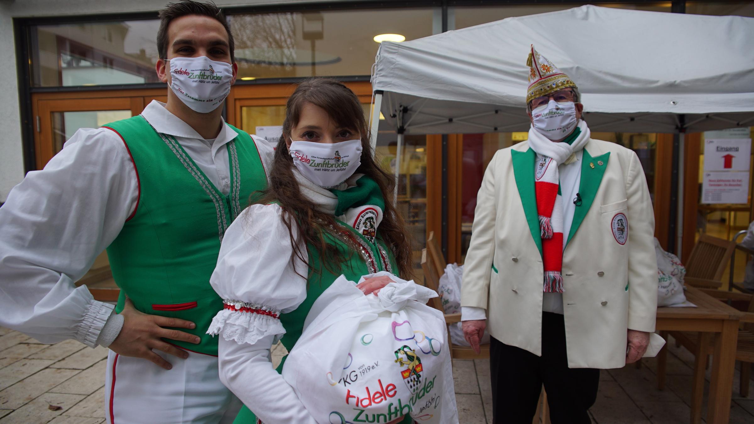 "ZDF.reportage: Wir machen weiter - trotz Corona! - Freizeit mit Maske": Michael G. und Ariane W. posieren in Kostümen. Ariane W. hält eine Tüte mit Kamellen. Etwas nach hinten versetzt steht Theo S.  vor einem weißen Pavillon.