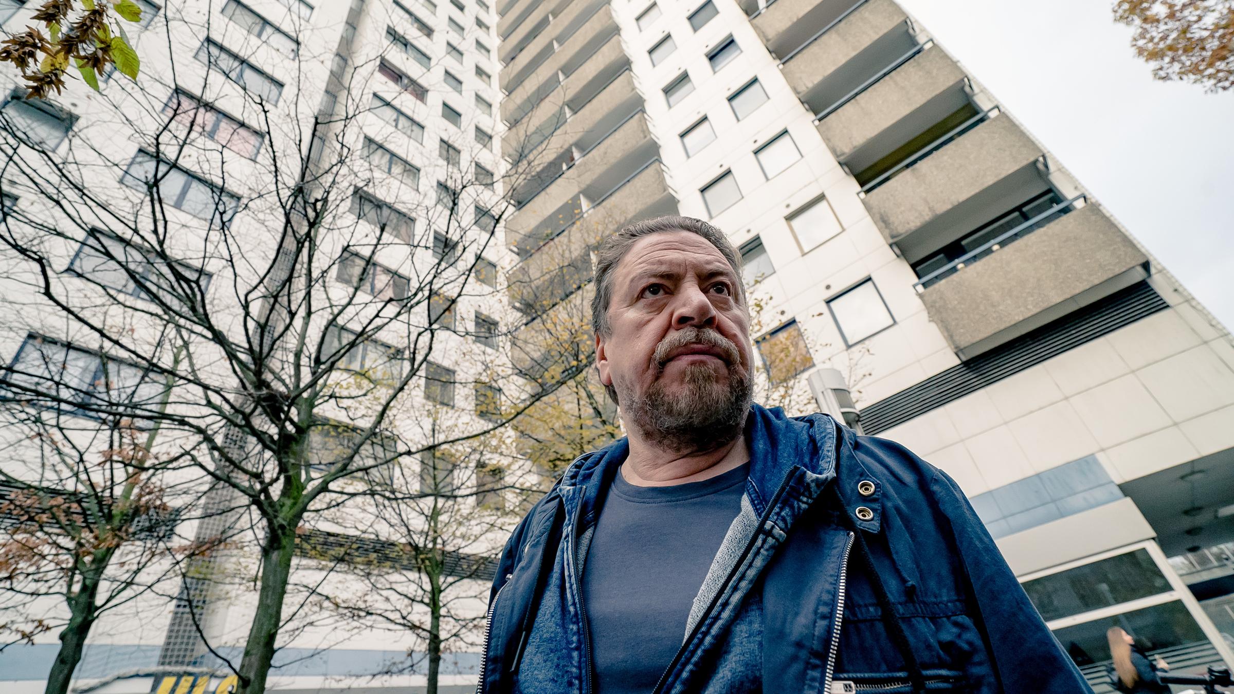 "Der gute Bulle - Nur Tote reden nicht": Fredo Schulz (Armin Rohde) blickt konzentriert geradeaus. Im Hintergrund sieht man ein großen Wohnkomplex und mehrere kahle Bäume.