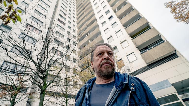 "Der gute Bulle - Nur Tote reden nicht": Fredo Schulz (Armin Rohde) blickt konzentriert geradeaus. Im Hintergrund sieht man ein großen Wohnkomplex und mehrere kahle Bäume.