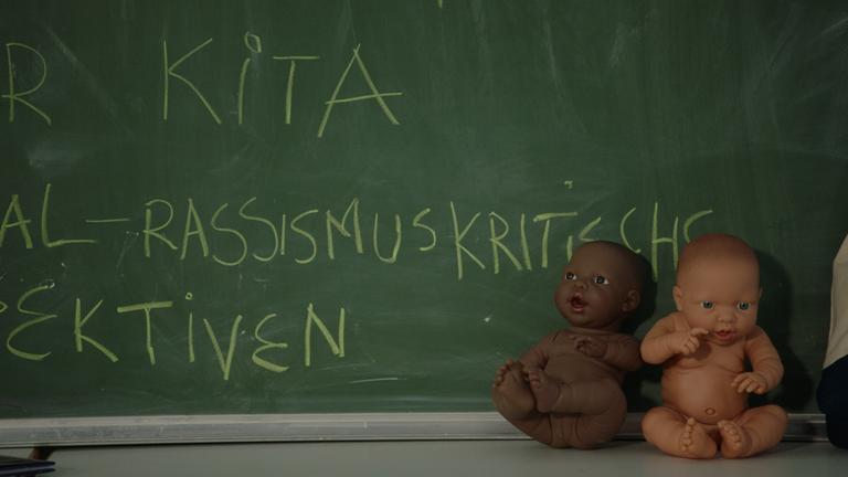 Die Macht der Vorurteile - Rassismus bewusst verlernen!: Zwei Puppen mit unterschiedlicher Hautfarbe sitzen vor einer Schultafel.