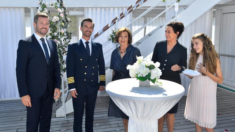 "Kreuzfahrt ins Glück - Hochzeitsreise nach Tirol": Hochzeitsplaner Tom (Jan Hartmann), Kapitän Max Parger (Florian Silbereisen), Kerstin Cramer (Gila von Weitershausen), Hanna Liebhold (Barbara Wussow) und Jette Herwig (Lola Höller) stehen in Abendgarderobe um einen hochzeitlich gedeckten Stehtisch.
