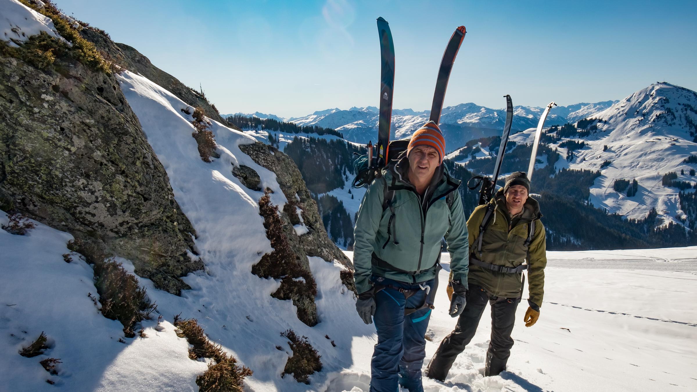 "Der Bergdoktor: Bauernopfer": In Winterausrüstung laufen Martin (Hans Sigl) und sein Bruder Hans (Heiko Ruprecht) einen schneebedeckten Berg hinauf. An ihren Rucksäcken auf dem Rücken sind ihre Skier angebracht.