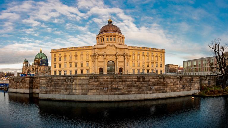 "ZDF.reportage: Prunk, Protz und Preußen - Das Berliner Schloss": Frontale Ansicht der Westfassade des Schlosses mit Kuppel vor blauem Himmel. Im Bilderhintergrund links sieht man den Berliner Dom. Im Vordergrund der Spreekanal.