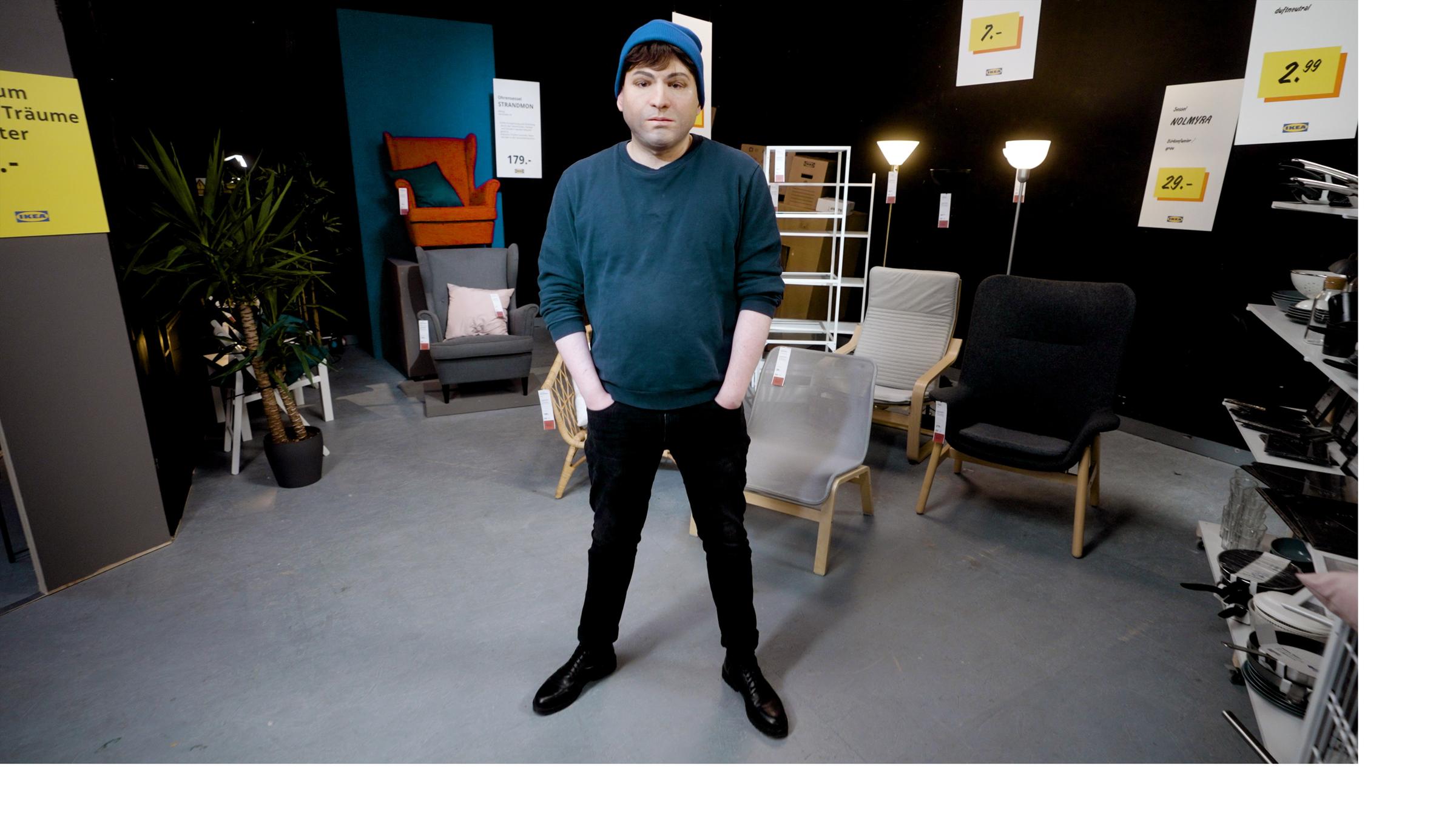 "ZDFzeit: IKEA: Die Insider - Verkaufstricks beim Möbel-Giganten": Ein ehemaliger Mitarbeiter von IKEA steht maskiert in einem Studio mit IKEA-Mobiliar.