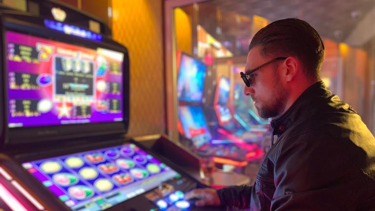 "37°: Verzockt - Wenn Glückspiel zur Sucht wird": Junger Mann sitzt in einer Spielhölle vor einem Spielautomaten und spielt.