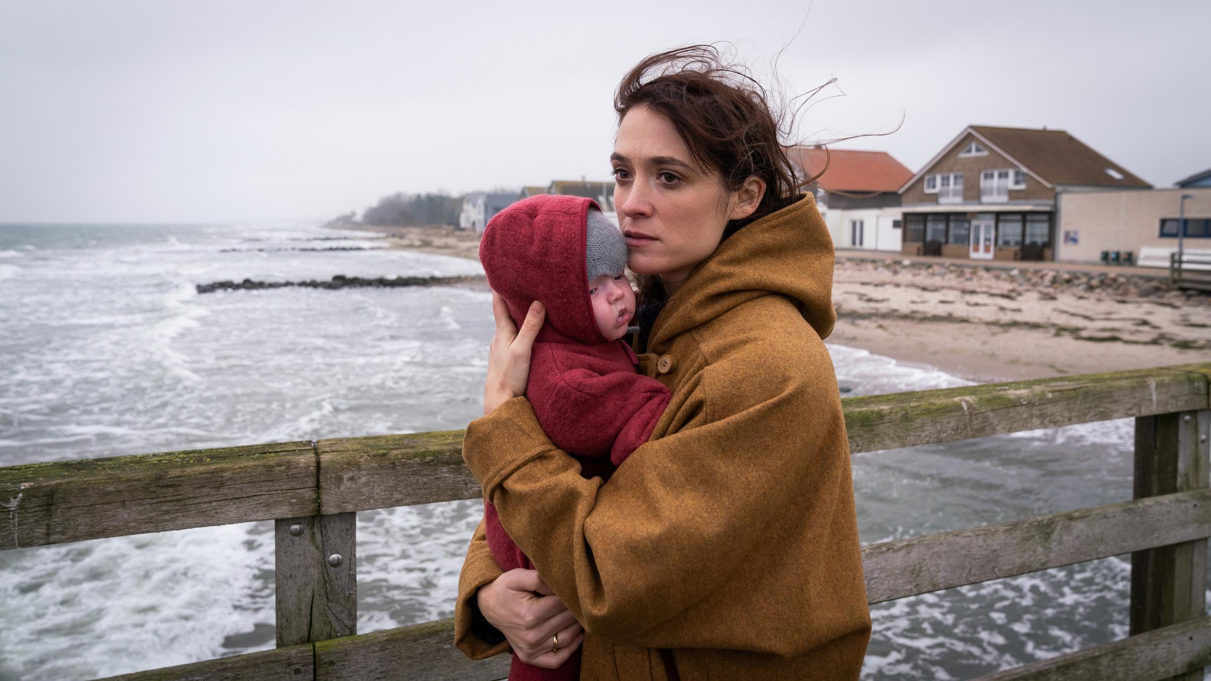 "Plötzlich so still": Eva (Friederike Becht) steht auf einer Seebrücke am Meer und hält ein Baby auf dem Arm.