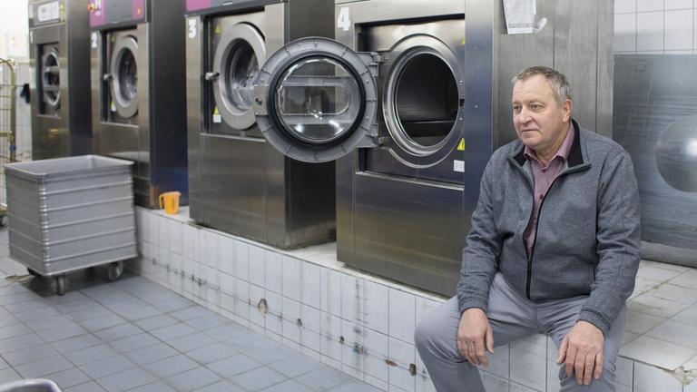 "37°: Unser verrücktes Jahr - Kleine Unternehmen in der Pandemie": Ein Mann sitzt in einer Wäscherei auf einem Wand, auf dem viele große Industrie-Waschmaschinen stehen.