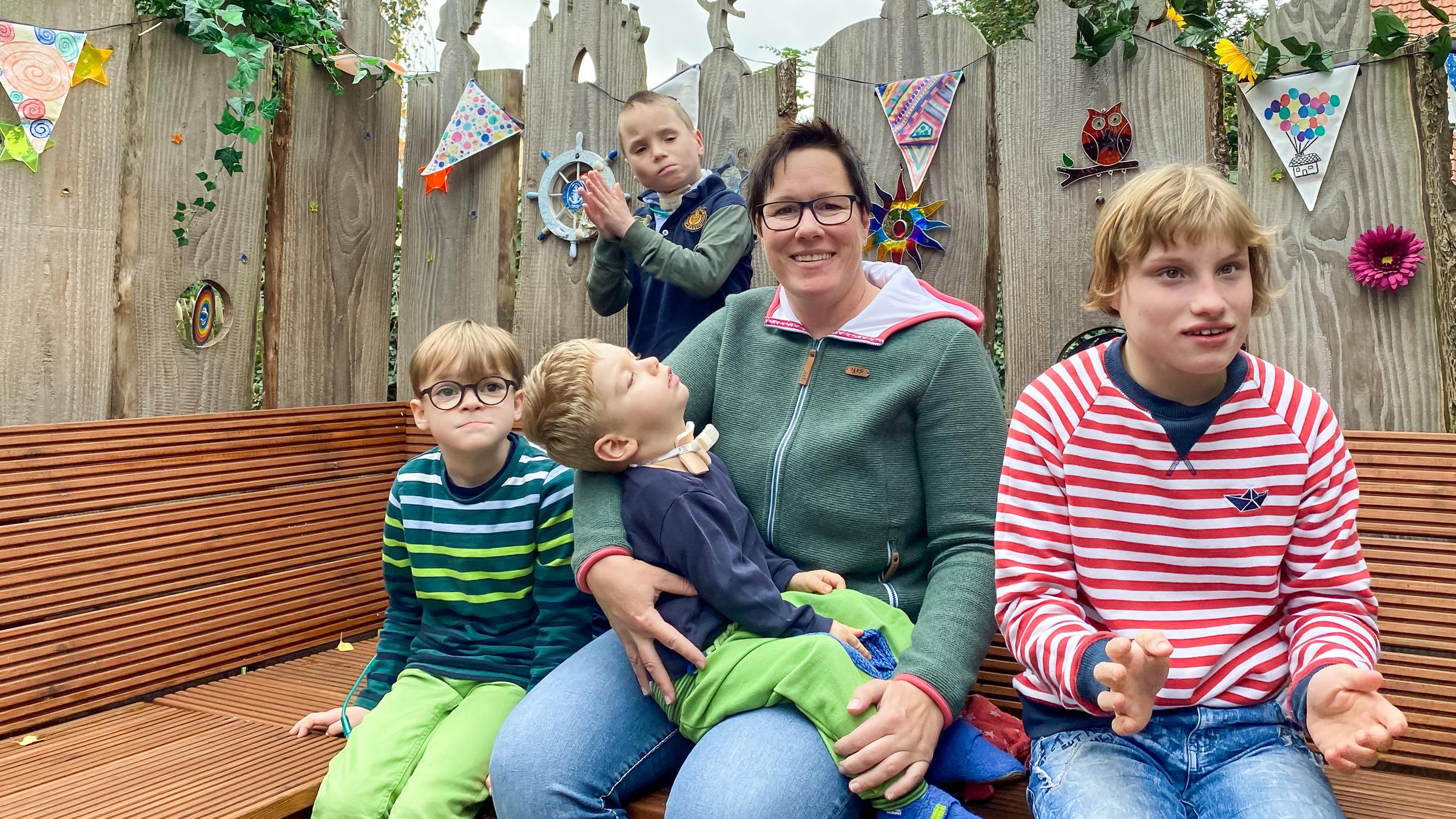 "37° Mama Held - Eine Pflegemutter kämpft für ihre Kinder": Eine Frau mittleren Alters mit kurzem dunklen Haar sitzt inmitten ihrer vier Pflegekinder auf einer Bank im Freien.