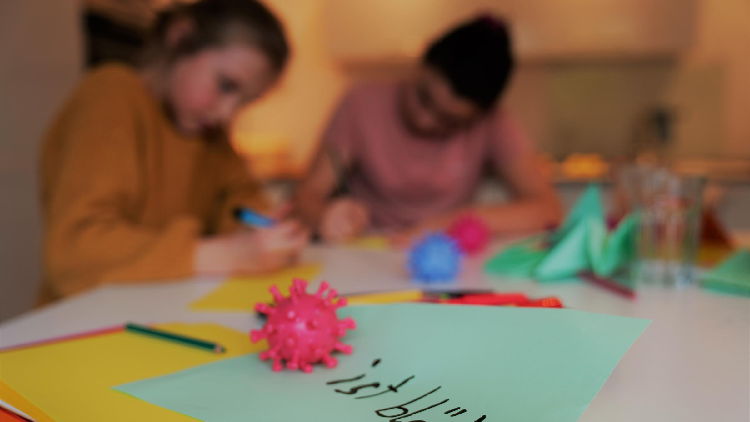 "ZDFzoom: Kinder im Shutdown - Abgehängt in der Krise": Zwei Mädchen sitzen an einem Tisch und schreiben. Im Vordergrund liegt ein roter Corona-Ball auf einem grünen Blatt Papier. Hinter dem Ball steht: "ist blöd!"