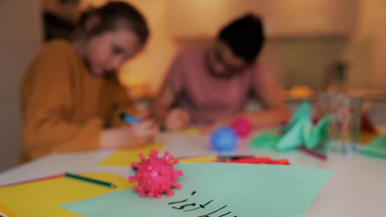 "ZDFzoom: Kinder im Shutdown - Abgehängt in der Krise": Zwei Mädchen sitzen an einem Tisch und schreiben. Im Vordergrund liegt ein roter Corona-Ball auf einem grünen Blatt Papier. Hinter dem Ball steht: "ist blöd!"
