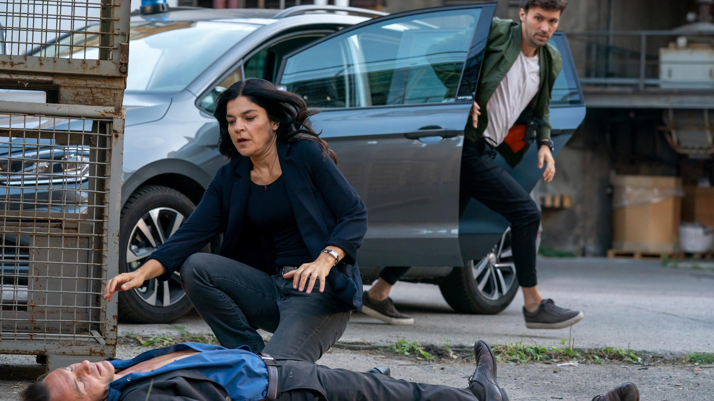 "Letzte Spur Berlin - Tag X - Teil 2": Mina (Jasmin Tabatabai) beugt sich über den am bodenliegenden Oliver Radek (Hans-Werner Meyer). Radek liegt ohnmächtig auf dem Boden. Sie sieht ängstlich aus. Alex (Aleksandar Radenković,) springt aus dem Auto und eilt zu ihr.