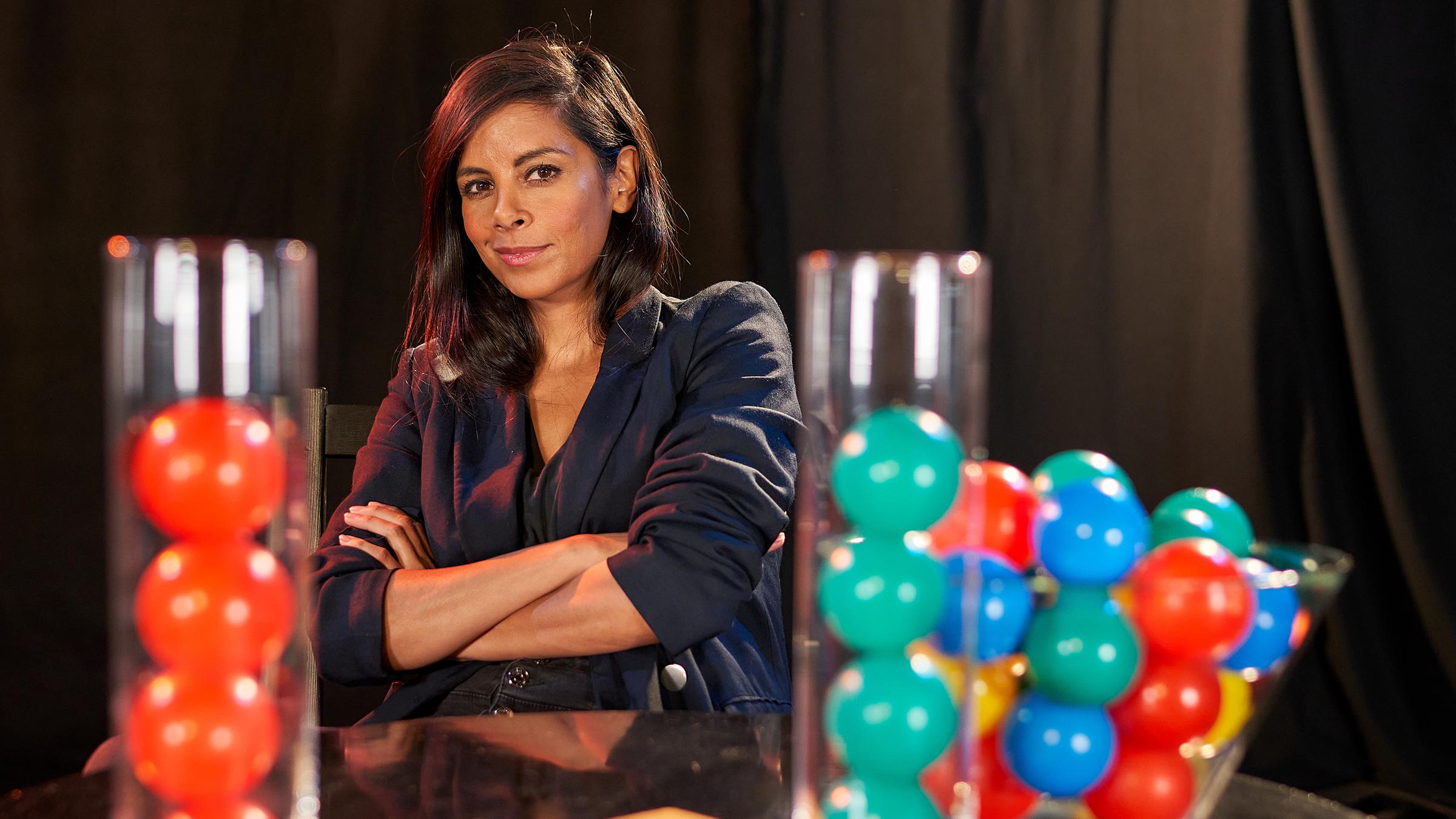 "Rabenmütter oder Super Moms? (2)": Die Moderatorin Collien Ulmen-Fernandes steht mit verschränkten Armen vor einen Stehtisch. Auf dem Tisch befinden sich Behälter, in denen bunte Bälle sind.