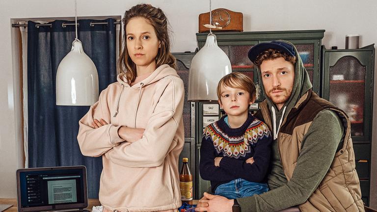 "Schlafschafe": Mutter Melanie (Lisa Bitter) steht mit verschränkten Armen neben ihrem Sohn Janosch (Emil Brosch) der bei Vater Lars (Daniel Donskoy) auf dem Schoß sitzt.