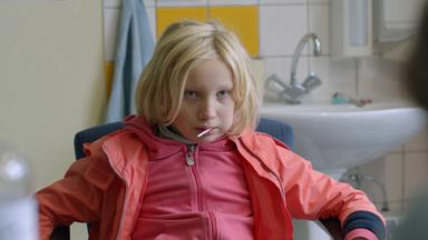 "Systemsprenger": Benni (Helena Zengel), ein neunjähriges blondes Mädchen, sitzt zurückgelehnt auf einem Stuhl , hat einen Lutscher im Mund und schaut eine ihr gegenüber sitzende Person verächtlich an.