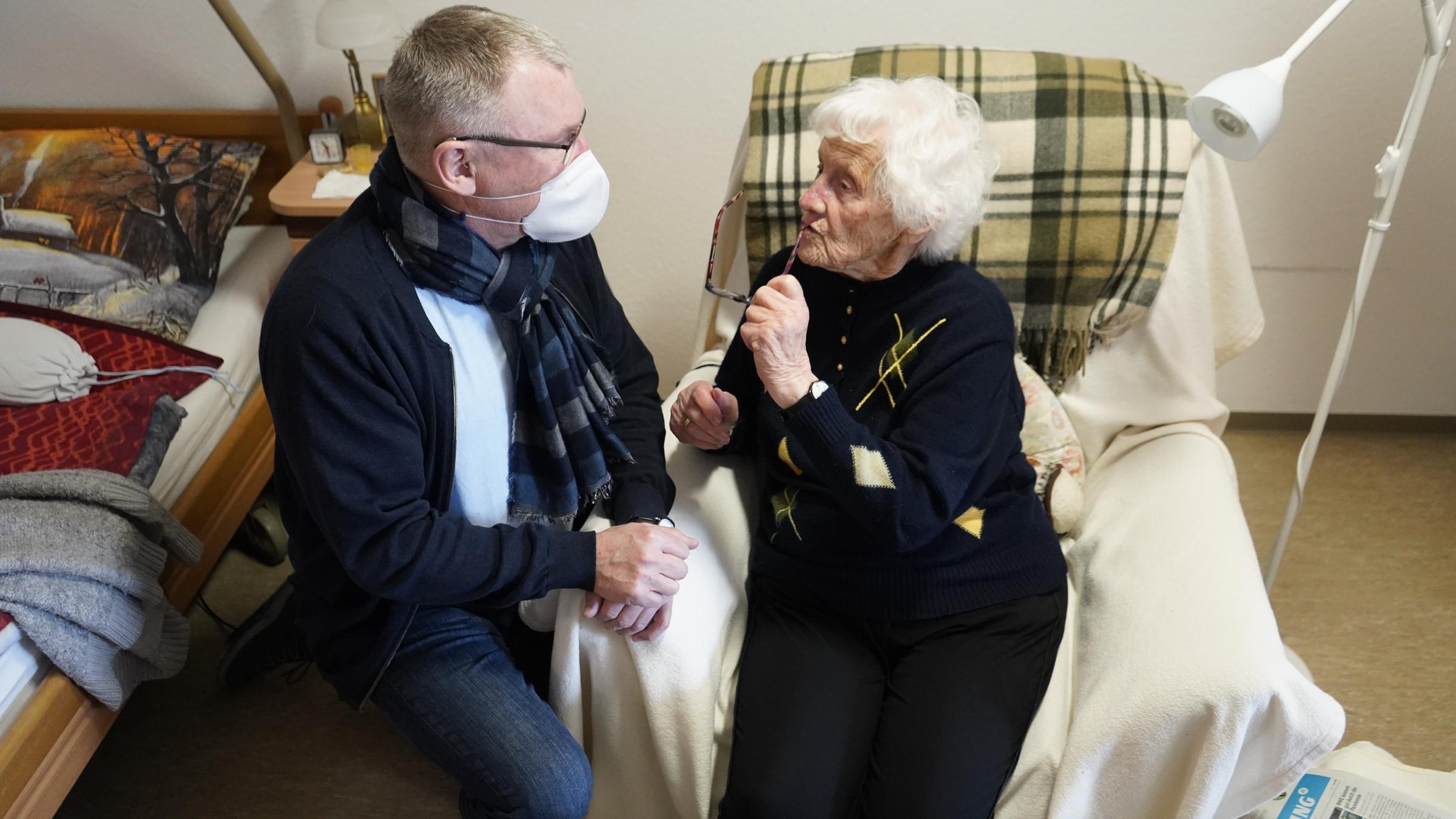 "ZDFzoom: Geimpft - und nun?": Der Heimleiter unterhält sich - sitzend zwischen Bett und Sessel - mit einer Seniorin.
