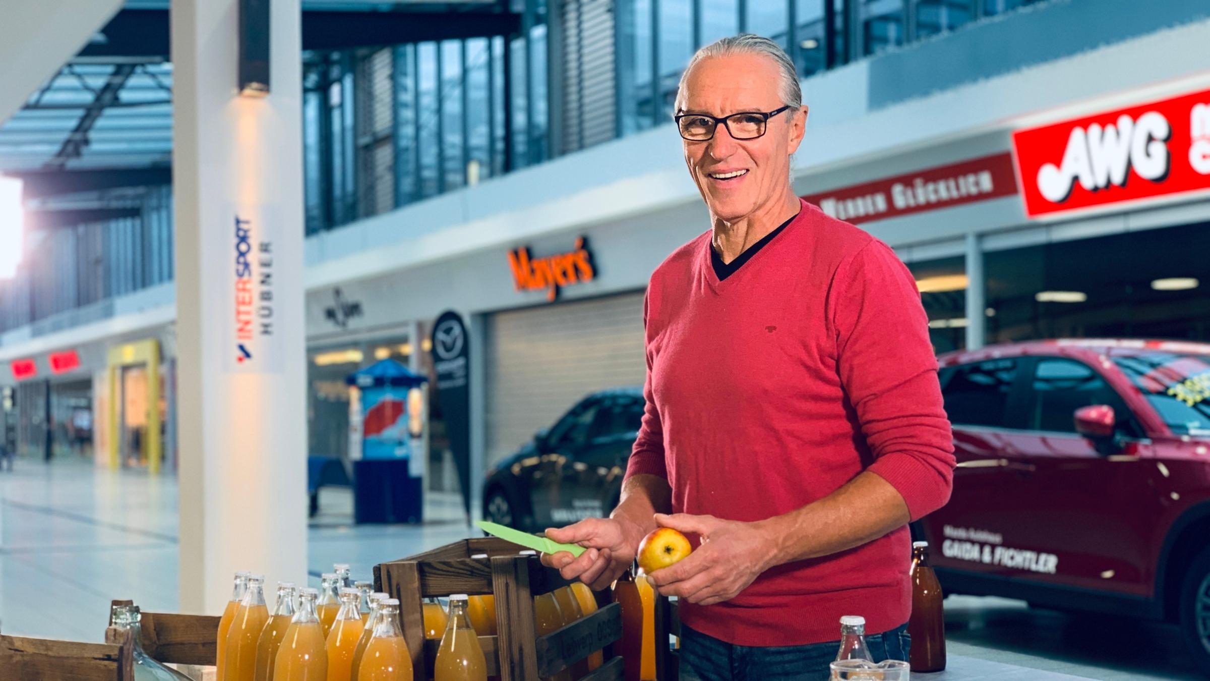 "ZDFzeit: Die Tricks des Einzelhandels - mit Eva Brenner": Lockvogel Reinhardt steht vor einem Stand mit Äpfeln und Apfelsaftflaschen und lächelt in die Kamera.