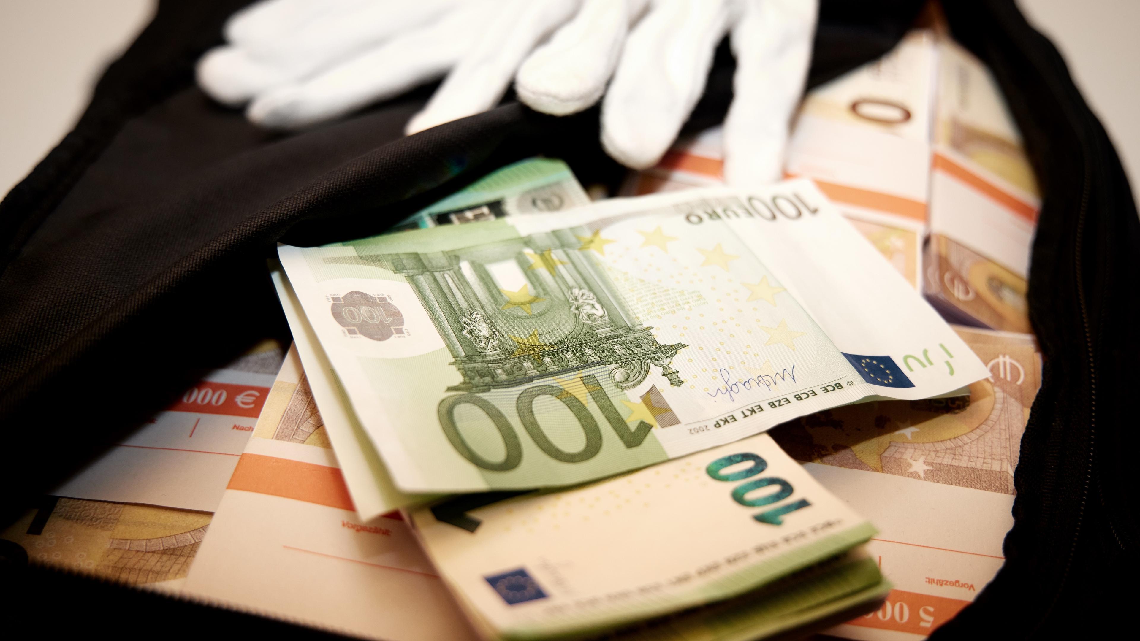 "ZDFzoom: Geldwäsche-Paradies Deutschland": In einer geöffneten schwarzen Tasche liegen Bündel von 100- und 50-Euro-Scheinen. Auf der Tasche liegt ein Paar weiße Handschuhe.