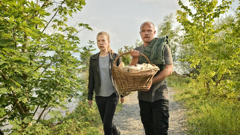"Die Toten vom Bodensee - Der Seelenkreis": Hannah Zeiler (Nora Waldstätten) und Micha Oberländer (Matthias Koeberlin) laufen nebeneinander über eine Wiese. Micha Oberländer (Matthias Koeberlin) hält einen Korb in der Hand.