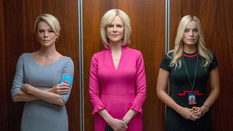 "Bombshell - Das Ende des Schweigens": Gretchen Carlson (Nicole Kidman), Megyn Kelly (Charlize Theron) und Kayla Pospisil (Margot Robbie) stehen nebeneinander in einem offenen Fahrstuhl und blicken den Betrachter an. Gretchen Carlson trägt ein auffälliges, pinkfarbenes Kleid.