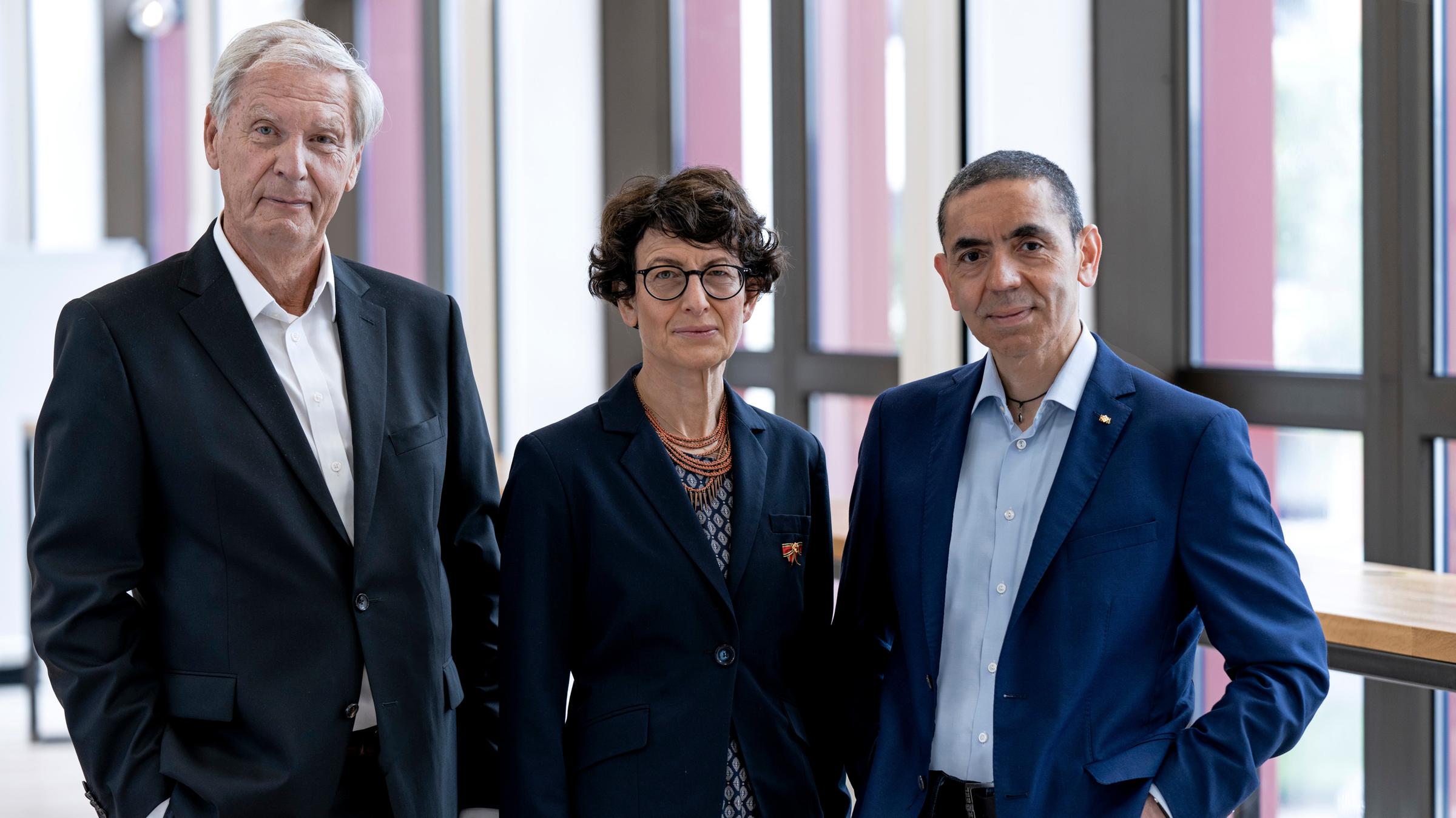 "Deutscher Zukunftspreis 2021 - Preis des Bundespräsidenten für Technik und Innovation":  Prof. Dr. med. Christoph Huber, PD Dr. med. Özlem Türeci, Prof. Dr. med. Uğur Şahin stehen in Business Kleidung nebeneinander und schauen freundlich in die Kamera