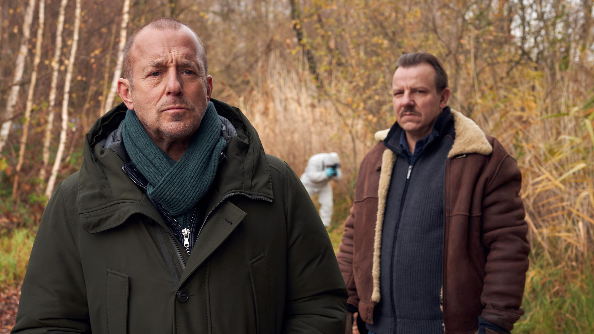 "Ingo Thiel - Ein Mädchen wird vermisst": Die beiden Ermittler Ingo Thiel (Heino Ferch) und Winni (Ronald Kukulies) stehen voreinander im Wald. Hinter ihnen ein Kollege von der Spurensicherung.