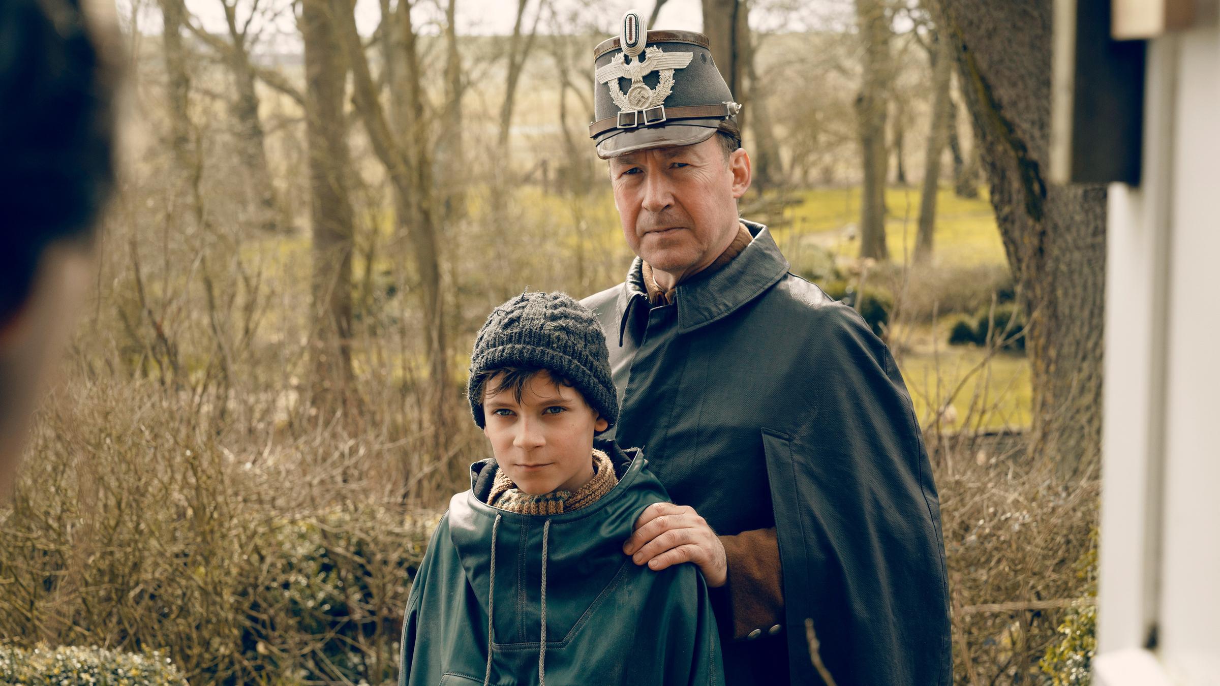 "Deutschstunde": Jens Ole Jepsen (Ulrich Noethen) und Siggi Jepsen (Levi Eisenblätter) stehen nebeneinander und schauen in die Kamera. Jens Ole hat seine Hände auf die Schultern seines Sohnes gelegt.