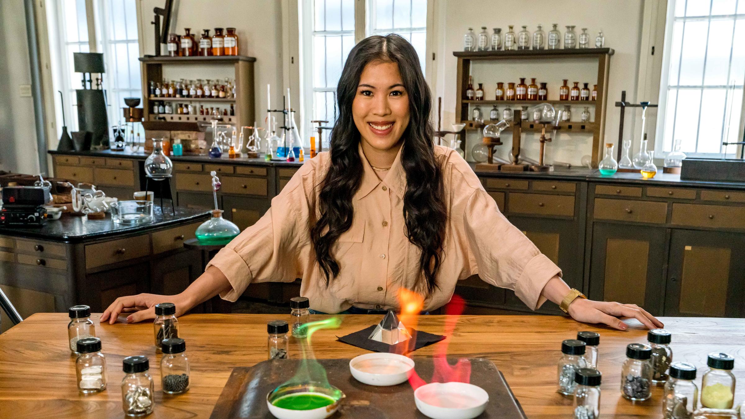 "Terra X: - Wunderwelt Chemie - Die Bausteine der Natur": Mai Thi Nguyen-Kim lehnt in einem alten Labor an einem Tisch. Vor ihr verschiedene Schalen mit chemischen Stoffen, die in grün, rot und gelb leuchten.