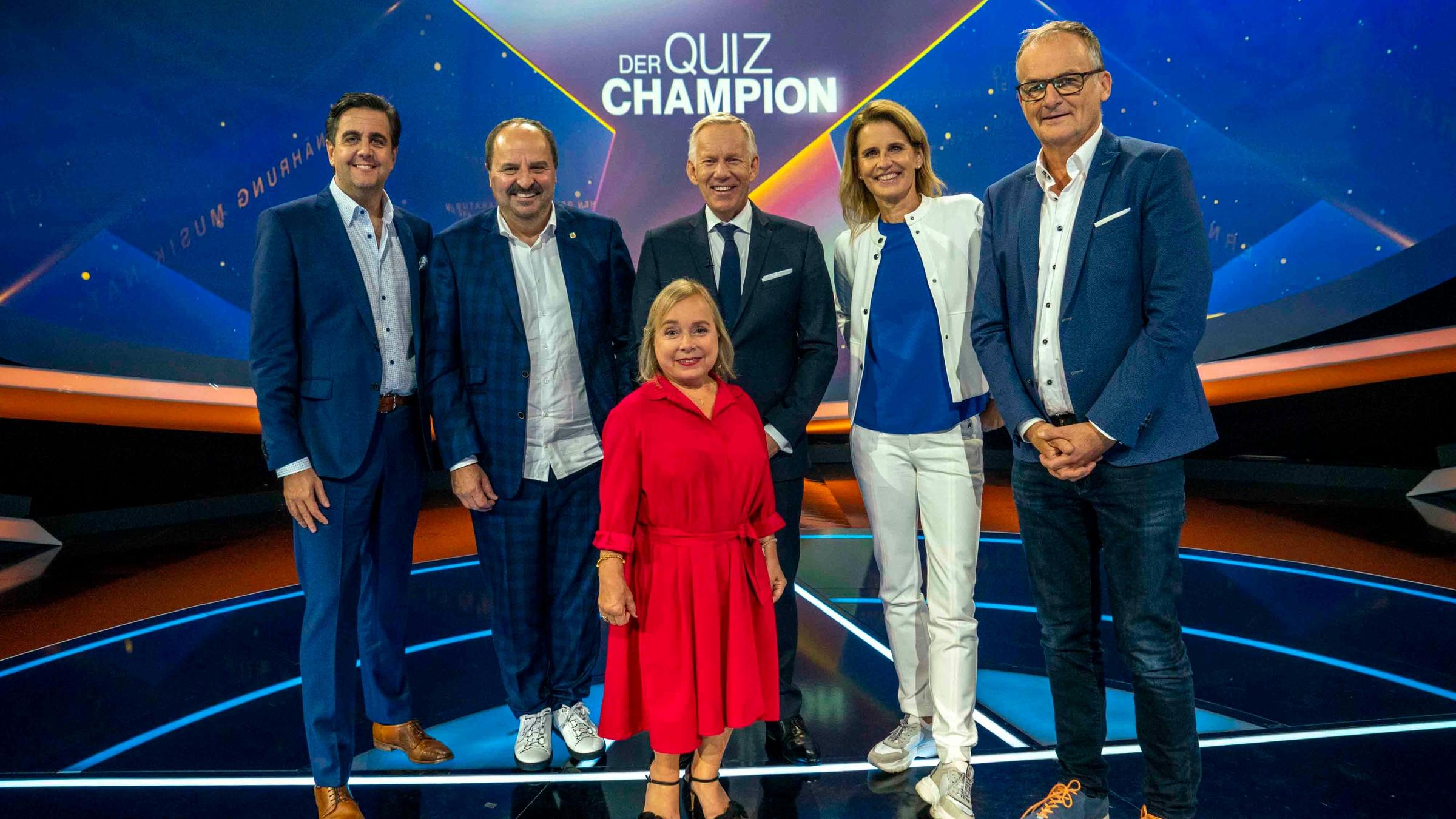 "Der Quiz-Champion": Johannes B. Kerner, ChrisTine Urspruch, Johann Lafer, Katrin Müller-Hohenstein, Bastian Pastewka und Frank Plasberg stehen im Studio vor "Quiz-Champion"-Logo und lächeln in die Kamera.