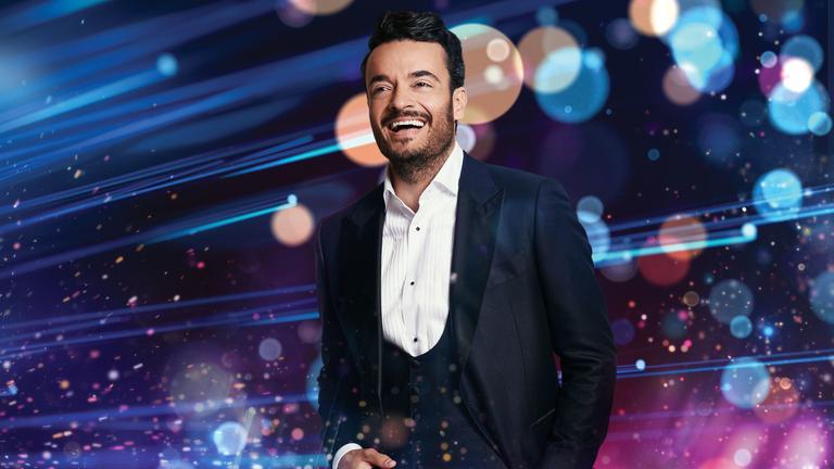  "Die Giovanni Zarrella Show": Giovanni Zarrella steht in einem dunklen Anzug vor Leuchteffekten und lächelt.