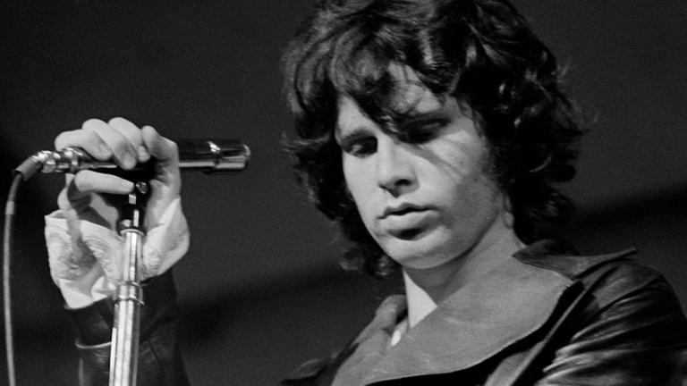 "The Day the Rock Star Died: Jim Morrison": Schwarz-Weiß-Foto von Jim Morrison bei einem Konzert. Er hält das Mikro in der Hand und hat die Augen geschlossen.