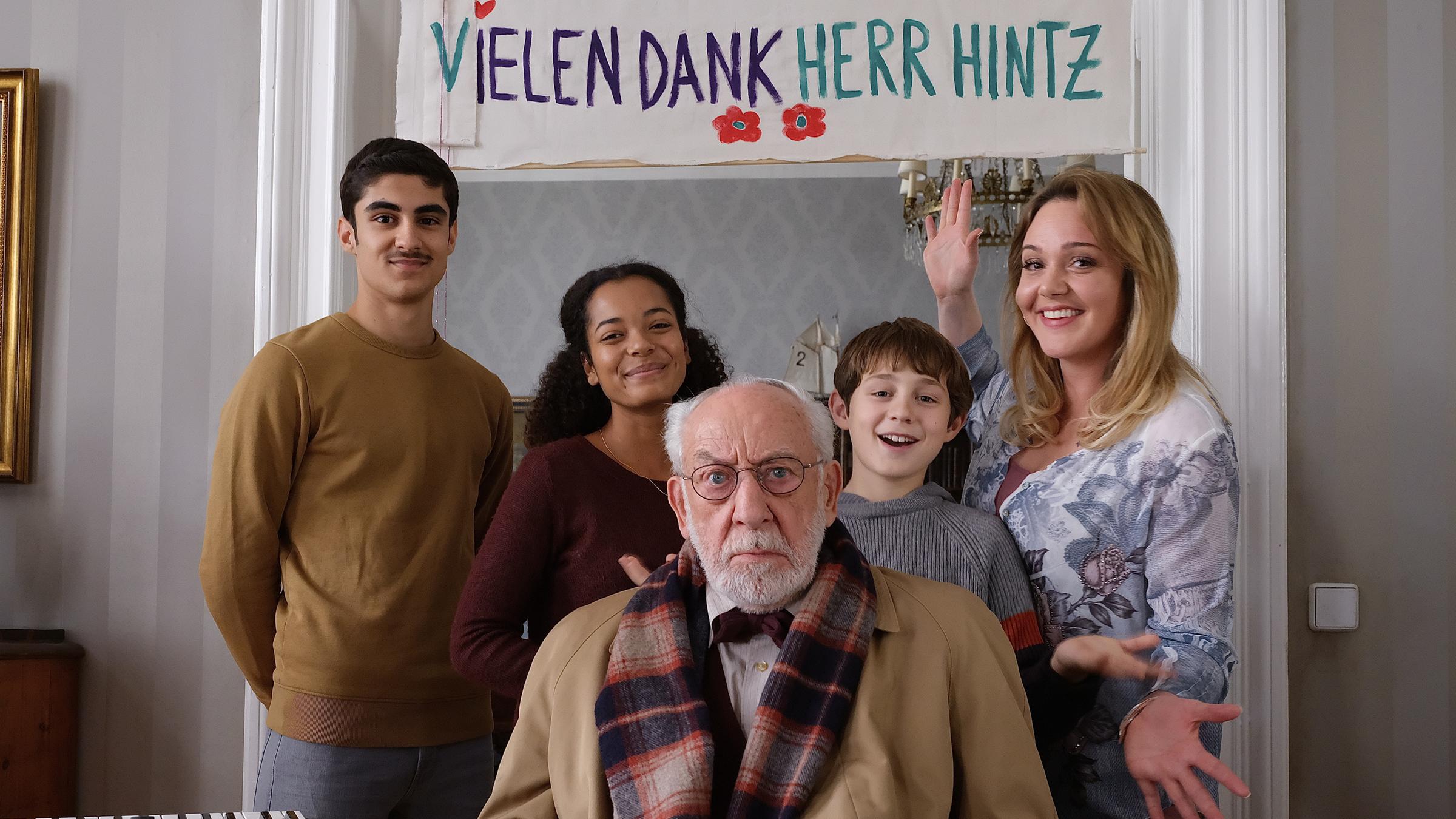 "Mein Freund, das Ekel - Voll verhintzt": Trixie Kuntze (Alwara Höfels) steht mit ihren Kindern Murat (Julius Gabriel Göze), Afia (Latisha Kohrs) und Sean (Lior Kudrjawizki) glücklich lachend und posierend beisammen. Olaf Hintz (Dieter Hallervorden) sitzt mit genervtem Blick vor den vier. Im Hintergrund hängt ein Plakat mit dem Schriftzug "Vielen Dank Herr Hintz".
